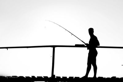 Silhouette man standing by railing against clear sky