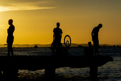 Silhouette people on beach against sky during sunset