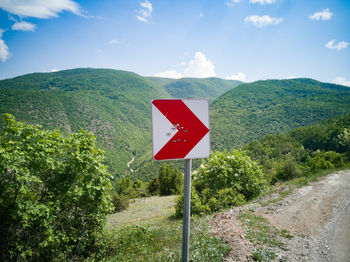 Road sign against trees and mountains against sky