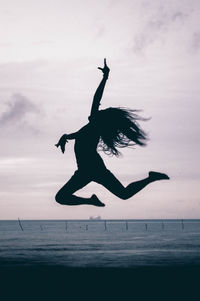 Silhouette woman jumping at beach against sky