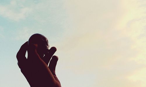 Low angle view of cropped hand holding skull against sky