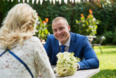 Smiling groom looking at bride sitting at table in park