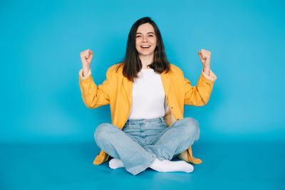 Portrait of young woman sitting against blue background