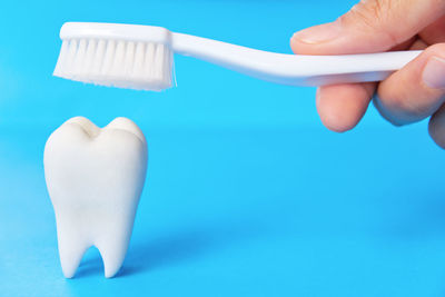 Cropped hand holding toothbrush over dentures against blue background