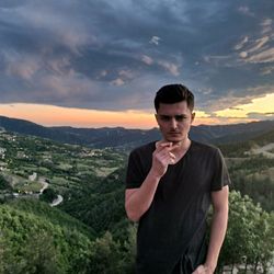 Young man standing on landscape against sky during sunset