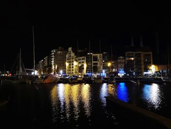 Illuminated buildings by river against clear sky at night