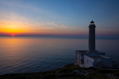 Lighthouse by sea against sky during sunset