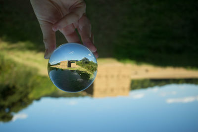 Close-up of man holding crystal ball against sky