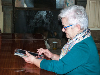 Side view of senior woman using digital tablet on table at home