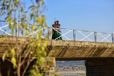 Low angle view of young couple on bridge against sky