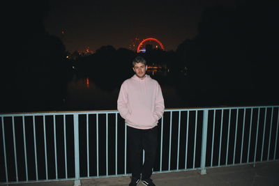 Man standing by railing against sky at night