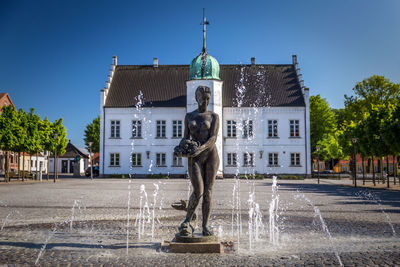Statue by fountain against building against sky