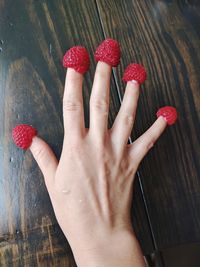 Cropped hand with raspberries at wooden table