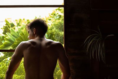 Rear view of shirtless man standing against plants
