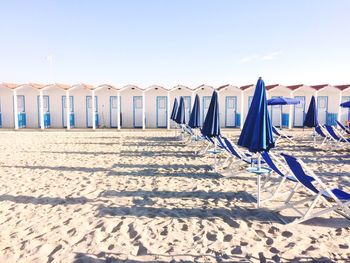 Blue umbrellas and deck chairs against huts at beach on sunny day