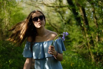 Teenage girl holding flower while tossing hair in forest