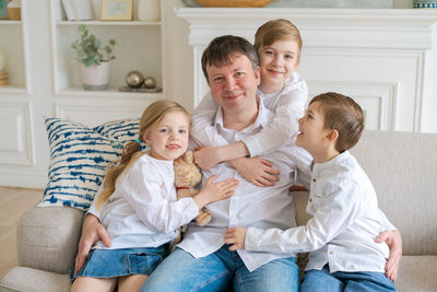 Happy father with three little children sitting on sofa looking at each other