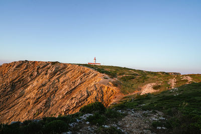 Lighthouse by mountain against clear blue sky