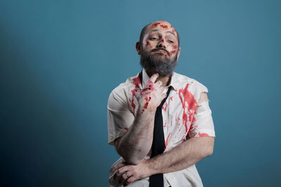 Portrait of senior man holding hands against blue background