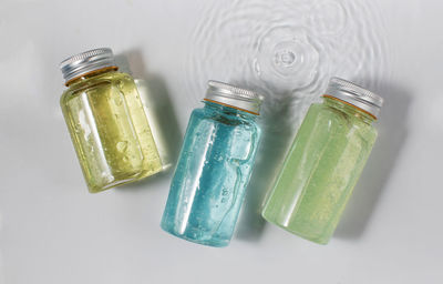 Bottles with multicolored gel skincare remedies on white surface with water