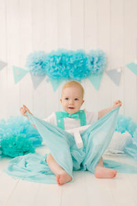 A beautiful one year old boy in turquoise clothes plays with a piece of blue cloth