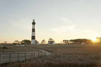 Lighthouse on field against cloudy sky