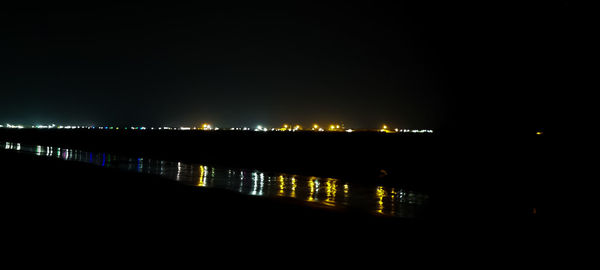 Illuminated city by river against sky at night