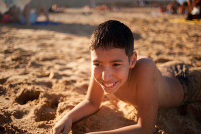 Close-up of smiling boy lying down on sand at beach