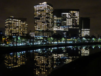 Illuminated buildings by river against sky at night