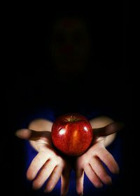 Close-up of hand holding apple over black background