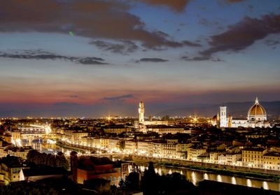 Illuminated buildings in city against sky during sunset