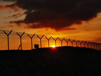 Silhouette fence against orange sky during sunset