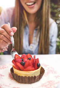 Young woman tasting strawberry-topped cake, selective focus.