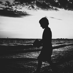 Silhouette boy standing on beach against sky during sunset