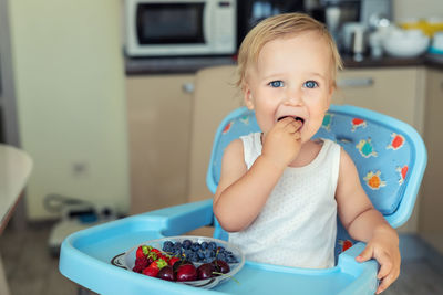 Portrait of cute baby boy eating cherry sitting at home