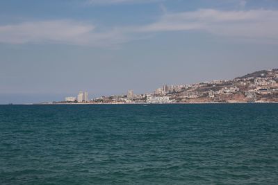 Sea by buildings in city against sky