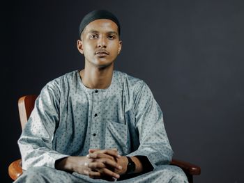 Portrait of young man sitting against black background