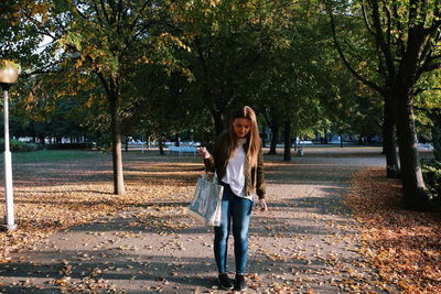 Full length of young woman standing on road at park during autumn