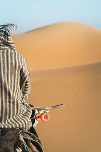 Rear view of man with skateboard sitting on camel during sunny day