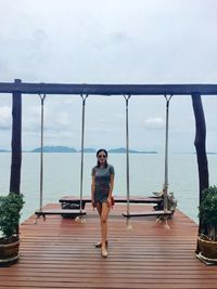 Full length of young woman standing amidst swings against sea