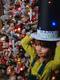 Girl wearing hat while standing by christmas tree at home