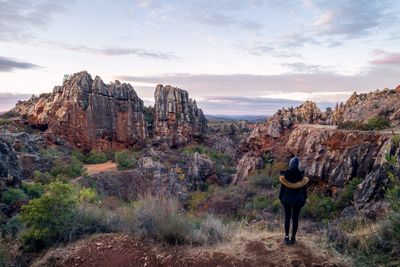 Rear view of woman standing on rock formation against sky