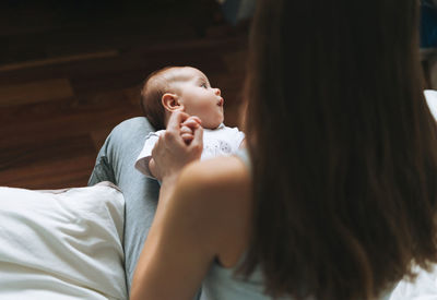 Young mother having fun with cute baby girl on her knees sitting on bed at home, love emotion