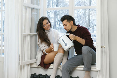 Side view of young woman sitting on window