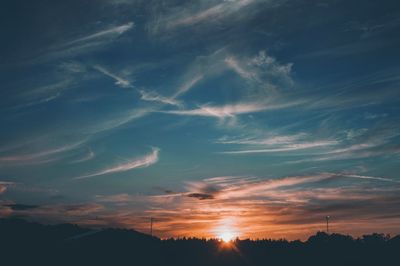 Low angle view of sunlight streaming through silhouette trees during sunset