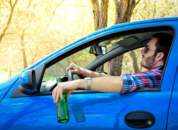 Man holding beer bottle while driving car in forest