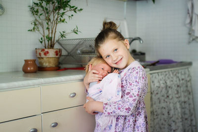 Cute european kid girl with baby doll in sling. motherhood and role-playing, child development