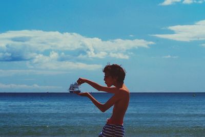 Shirtless boy standing at beach against sky