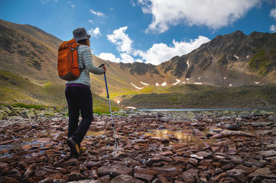 A stylishly dressed woman goes with trekking poles and a backpack to a mountain lake. hiking in the