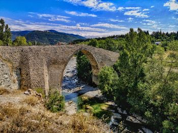 Arch bridge over river against cloudy sky